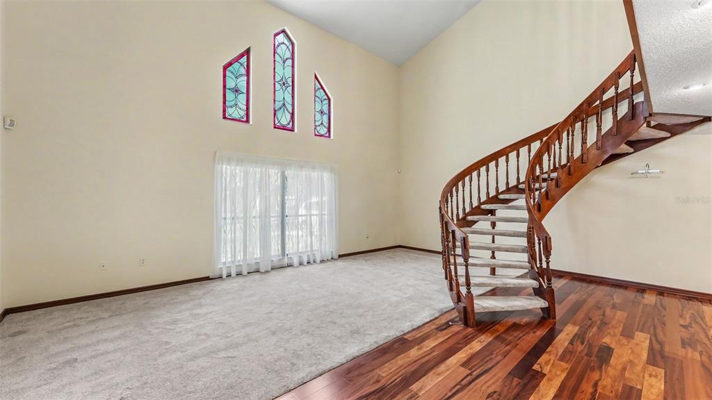 A living room features a curved wooden staircase, carpeted flooring, and three tall stained-glass windows — 633 VICTORIA SQUARE LANE, LAKELAND, FL