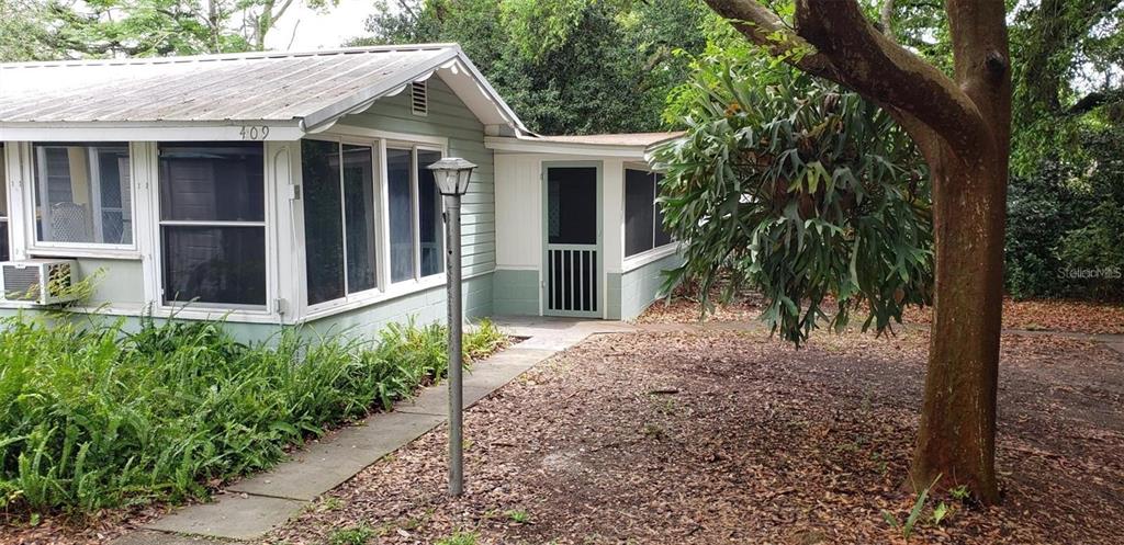 A light green house with a metal roof and a screened-in porch stands near trees — 409 W PEARL STREET, CLERMONT, FL