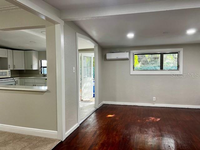 A living room with dark wood floors, a wall-mounted air conditioner, and an adjacent kitchen — 409 W PEARL STREET, CLERMONT, FL