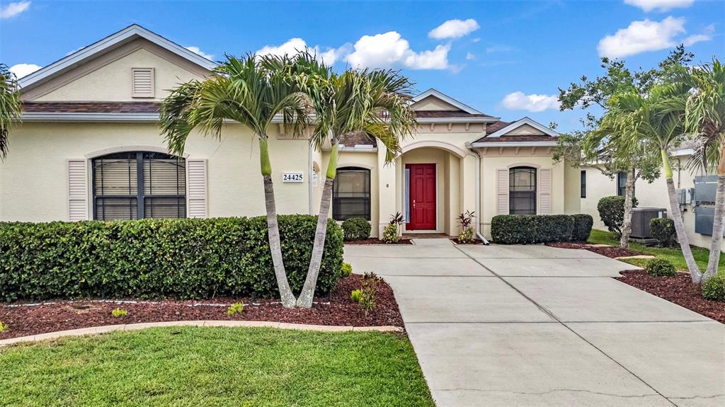A single-story house with a red front door, palm trees, and a concrete driveway — 24425 LAKEVIEW PLACE, PORT CHARLOTTE, FL