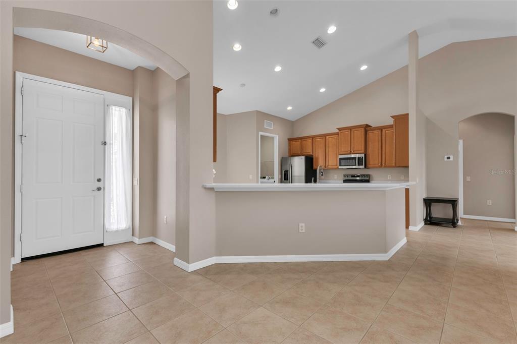 An open-concept kitchen with wood cabinets and a breakfast bar overlooks a tiled entryway — 24425 LAKEVIEW PLACE, PORT CHARLOTTE, FL