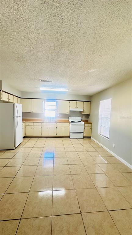 A kitchen features beige tile flooring, white appliances, and light-colored wooden cabinets — 1229 KENNEDY ROAD UNIT 62, DAYTONA BEACH, FL
