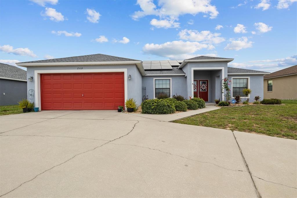 A single-story house with a red garage door, gray siding, and solar panels on the roof — 2559 SUNSET CIRCLE, LAKE WALES, FL