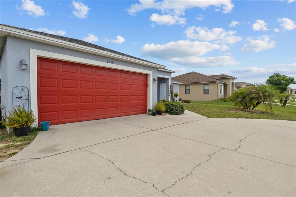 A house with a red garage door and a concrete driveway under a blue sky — 2559 SUNSET CIRCLE, LAKE WALES, FL