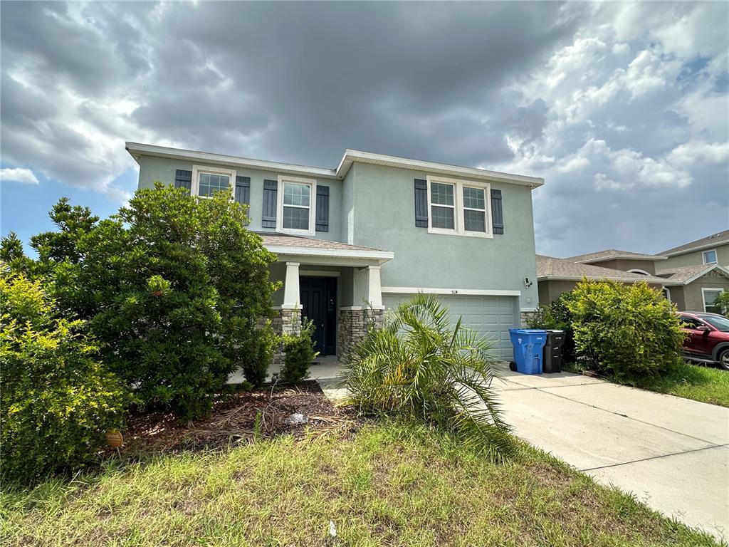 A two-story house with light green stucco siding, stone accents, and a two-car garage — 5114 JACKEL CHASE DRIVE, WIMAUMA, FL
