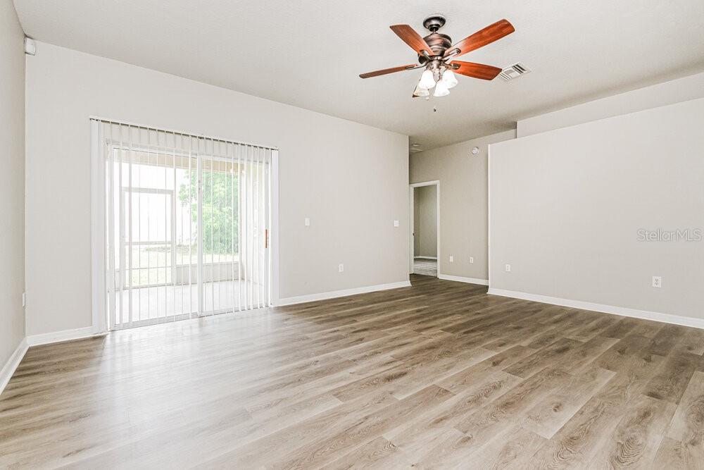 An empty living room features wood-look flooring, a ceiling fan, and sliding glass patio doors — 292 CLOVERDALE ROAD, WINTER HAVEN, FL
