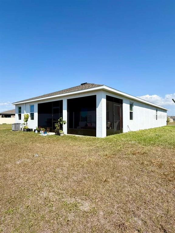 The rear exterior of a single-story house features a screened-in lanai and a grassy yard — 5452 FLINT HILLS DRIVE, WIMAUMA, FL
