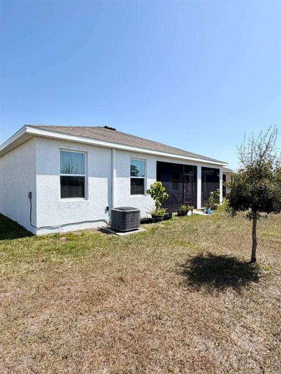 The back exterior of a white stucco house features a screened-in porch and air conditioner — 5452 FLINT HILLS DRIVE, WIMAUMA, FL