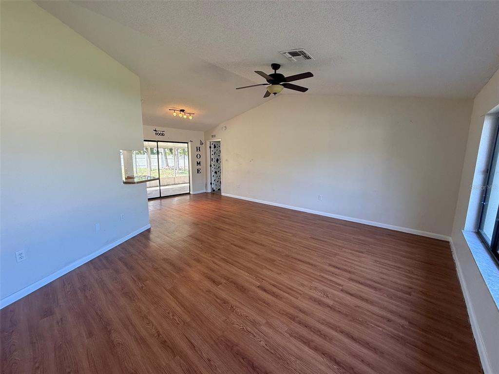 An empty living room features wood-look flooring, a vaulted ceiling with a fan, and sliding doors — 14078 SPRING HILL DRIVE, SPRING HILL, FL