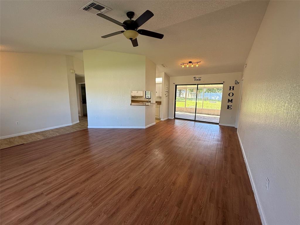 A spacious living area features wood-look flooring, a ceiling fan, and sliding glass patio doors — 14078 SPRING HILL DRIVE, SPRING HILL, FL