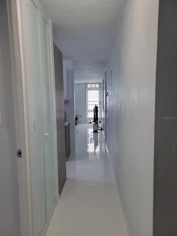 A narrow hallway with white tile flooring leads toward a doorway with a security gate — B4 ST GUATEMALA UNIT B4, HUMACAO, PR