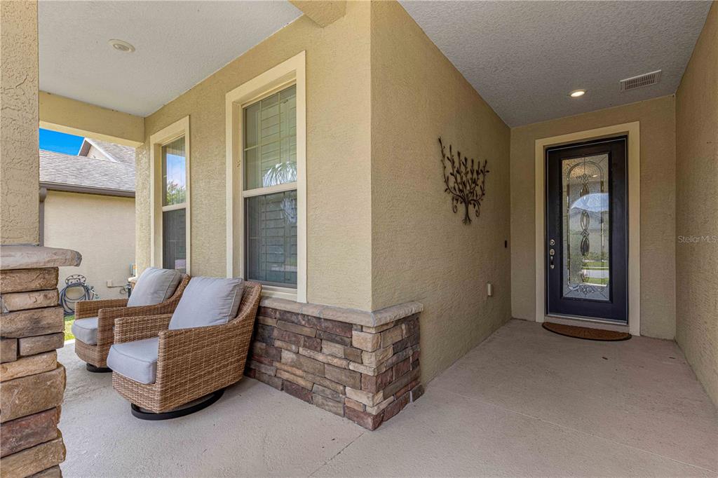 A covered front porch features two wicker chairs, stone accents, and a glass-paneled front door — 9793 SW 63RD LOOP, OCALA, FL