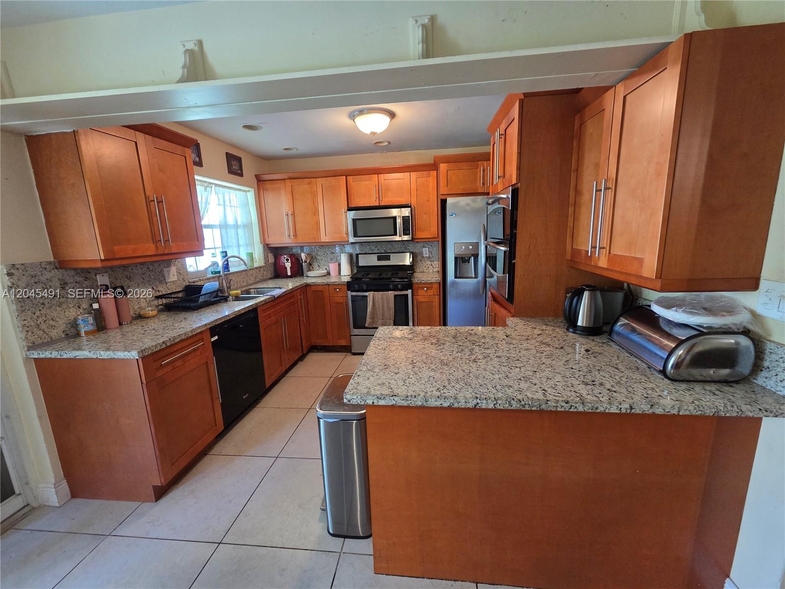 A kitchen features wood cabinets, granite countertops, stainless steel appliances, and light-colored tile flooring — 12061 SW 119th St, Miami FL 33186, MIAMI, FL