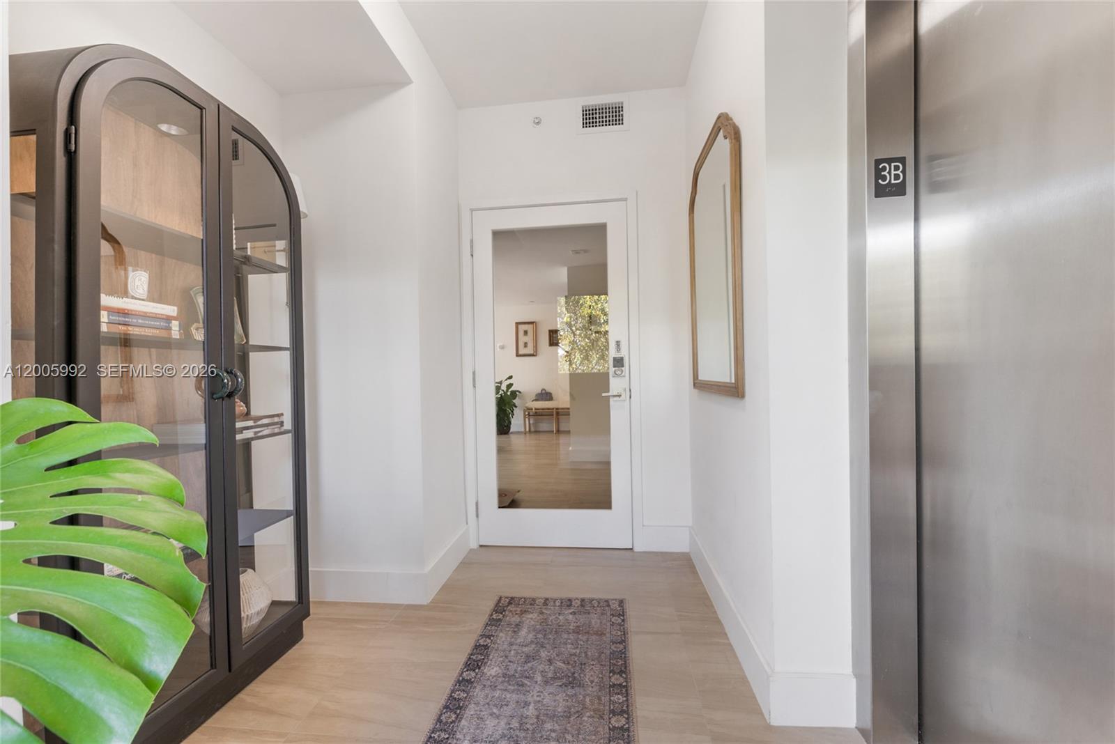 A hallway features a glass-front cabinet, a runner rug, a mirror, and an elevator door — 120 Salamanca Ave # 3B, Coral Gables FL 33134, CORAL GABLES, FL