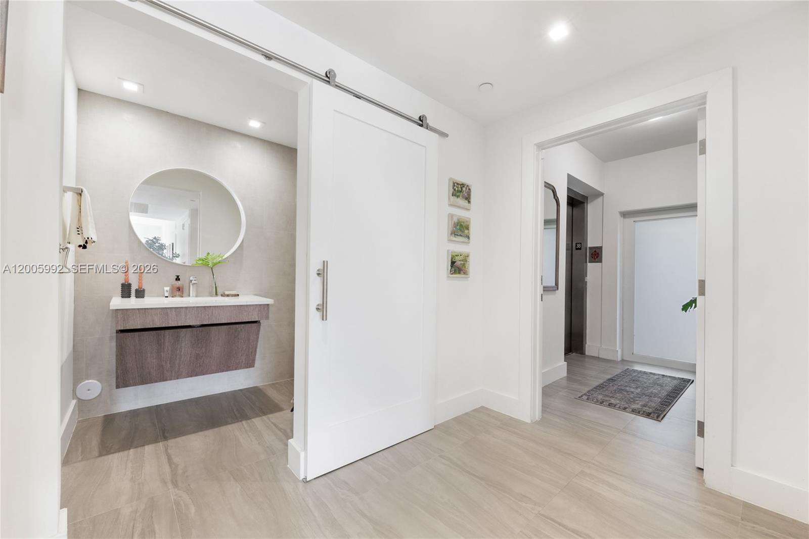 A modern bathroom with a floating vanity and circular mirror sits beside a hallway entrance — 120 Salamanca Ave # 3B, Coral Gables FL 33134, CORAL GABLES, FL