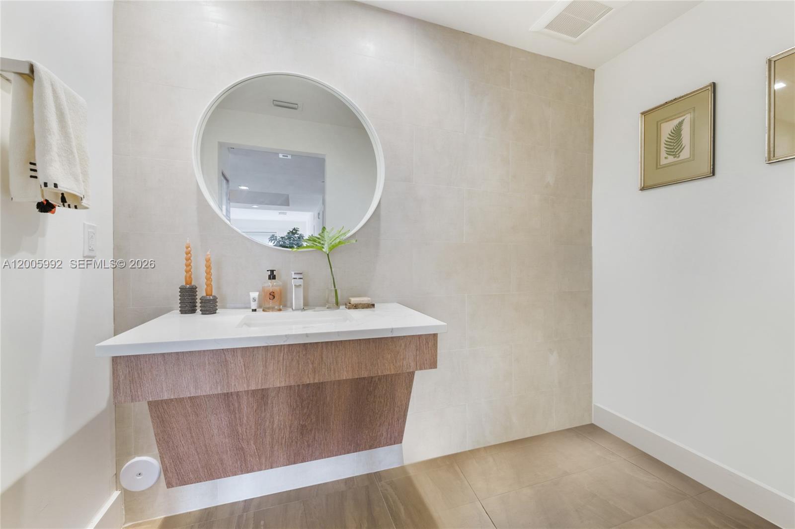 A modern bathroom features a floating wood vanity, a round mirror, and neutral tile walls — 120 Salamanca Ave # 3B, Coral Gables FL 33134, CORAL GABLES, FL