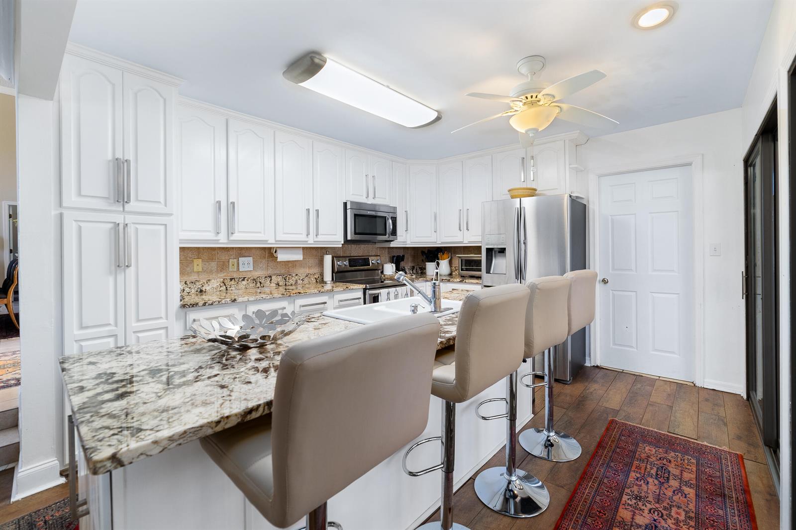 A kitchen features white cabinetry, granite countertops, stainless steel appliances, and a breakfast bar — 3000 Conifer Drive, Fort Pierce FL 34951, FORT PIERCE, FL