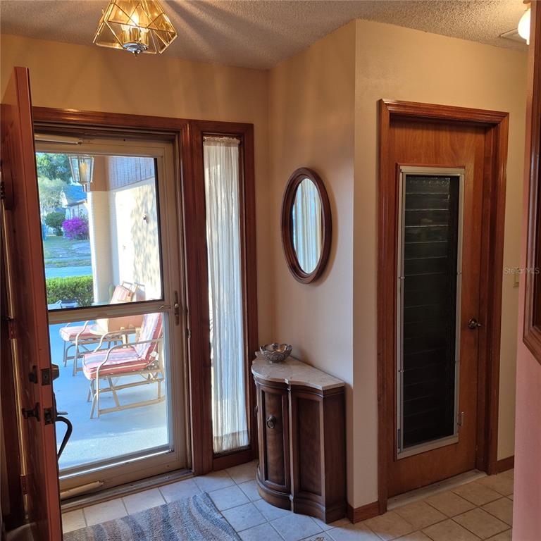 An entryway features a tiled floor, a wooden door with a screen, and a small console — 7828 ROYAL STEWART DRIVE, NEW PORT RICHEY, FL