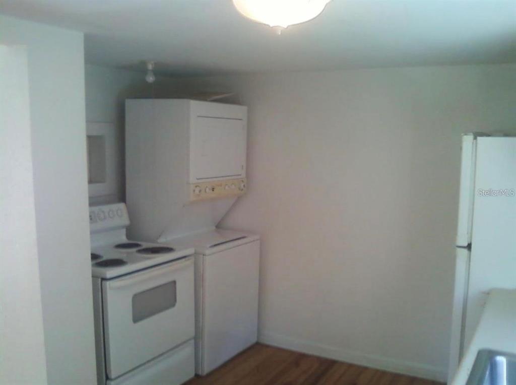 A kitchen features a white stove, a stacked washer and dryer, and a refrigerator — 7205 S MANHATTAN AVENUE, TAMPA, FL