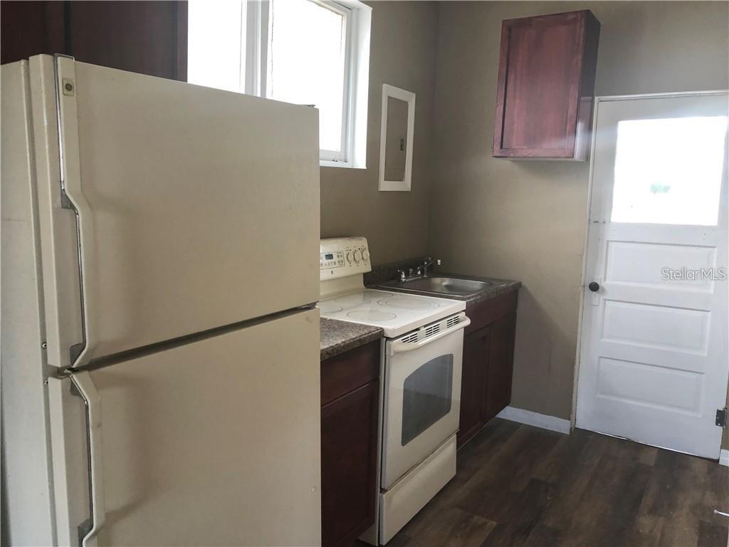A kitchen features a white refrigerator, a white stove, dark cabinets, and a back door — 1117 11TH STREET, ST CLOUD, FL