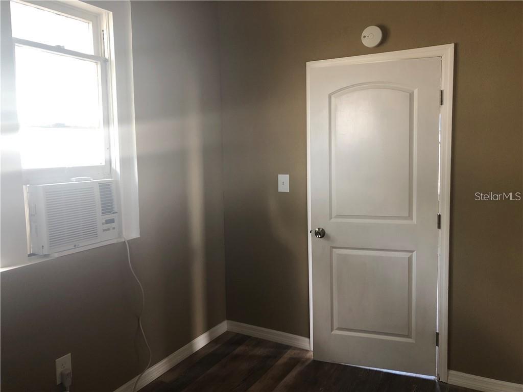 A room with dark walls, wood-look flooring, a window air conditioner, and a white door — 1117 11TH STREET, ST CLOUD, FL