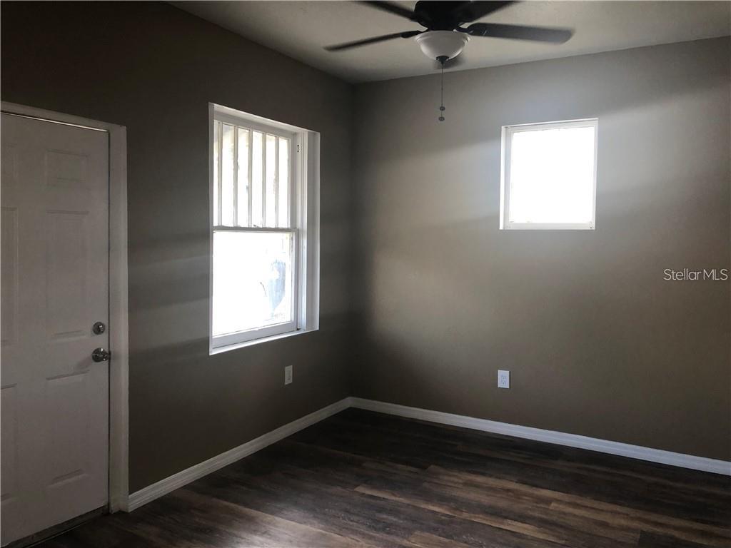 An empty room features dark wood-look flooring, gray walls, a ceiling fan, and two windows — 1117 11TH STREET, ST CLOUD, FL