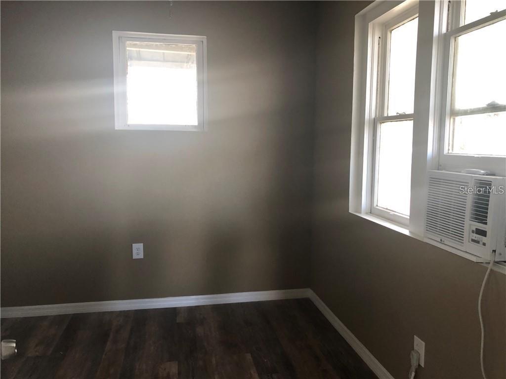 An empty room features dark wood-look flooring, gray walls, a small window, and an air conditioner — 1117 11TH STREET, ST CLOUD, FL