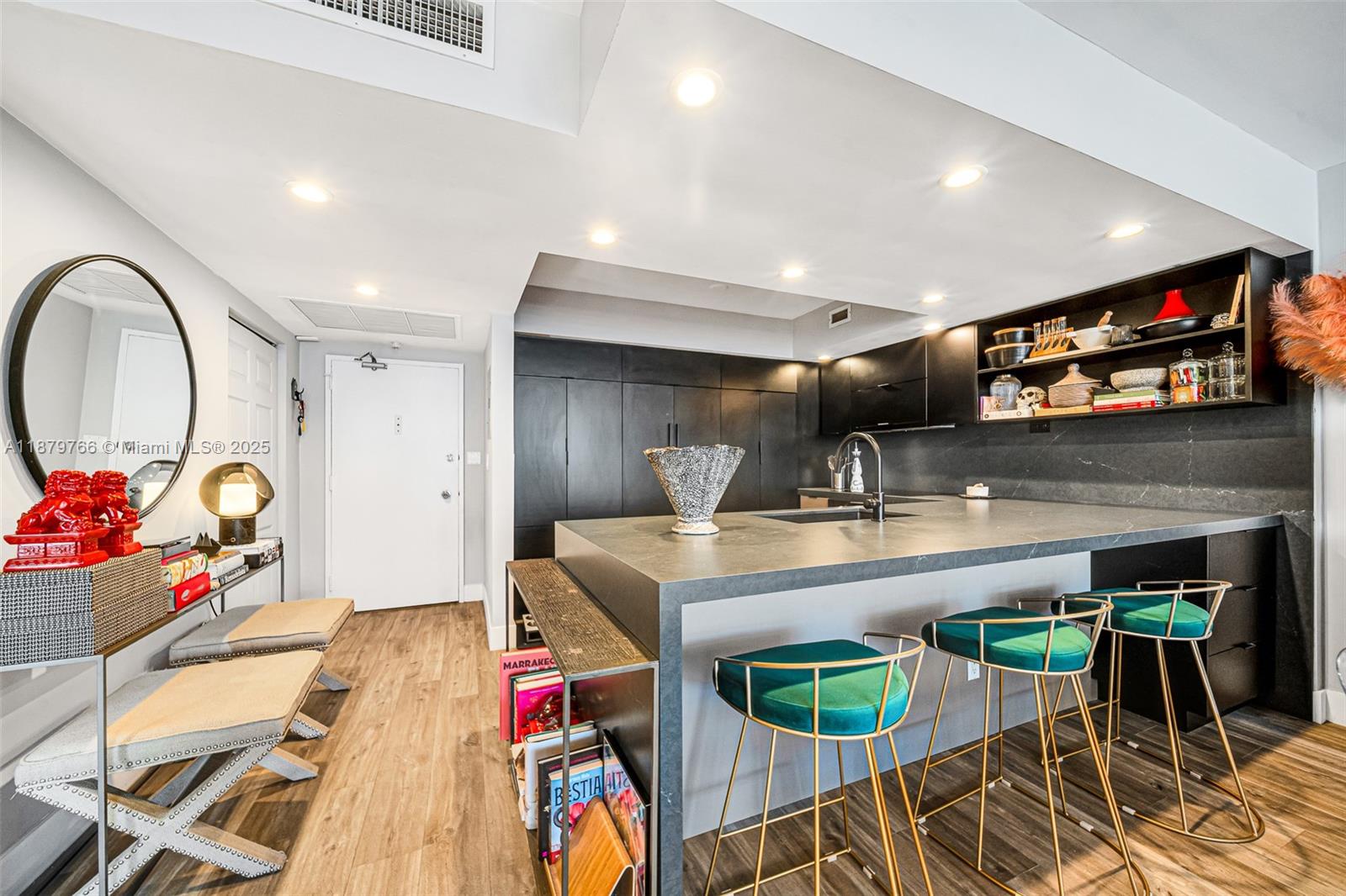 A modern kitchen features dark cabinetry, a stone island with green stools, and wood flooring — 5600 Collins Ave # 12E, Miami Beach FL 33140, MIAMI BEACH, FL