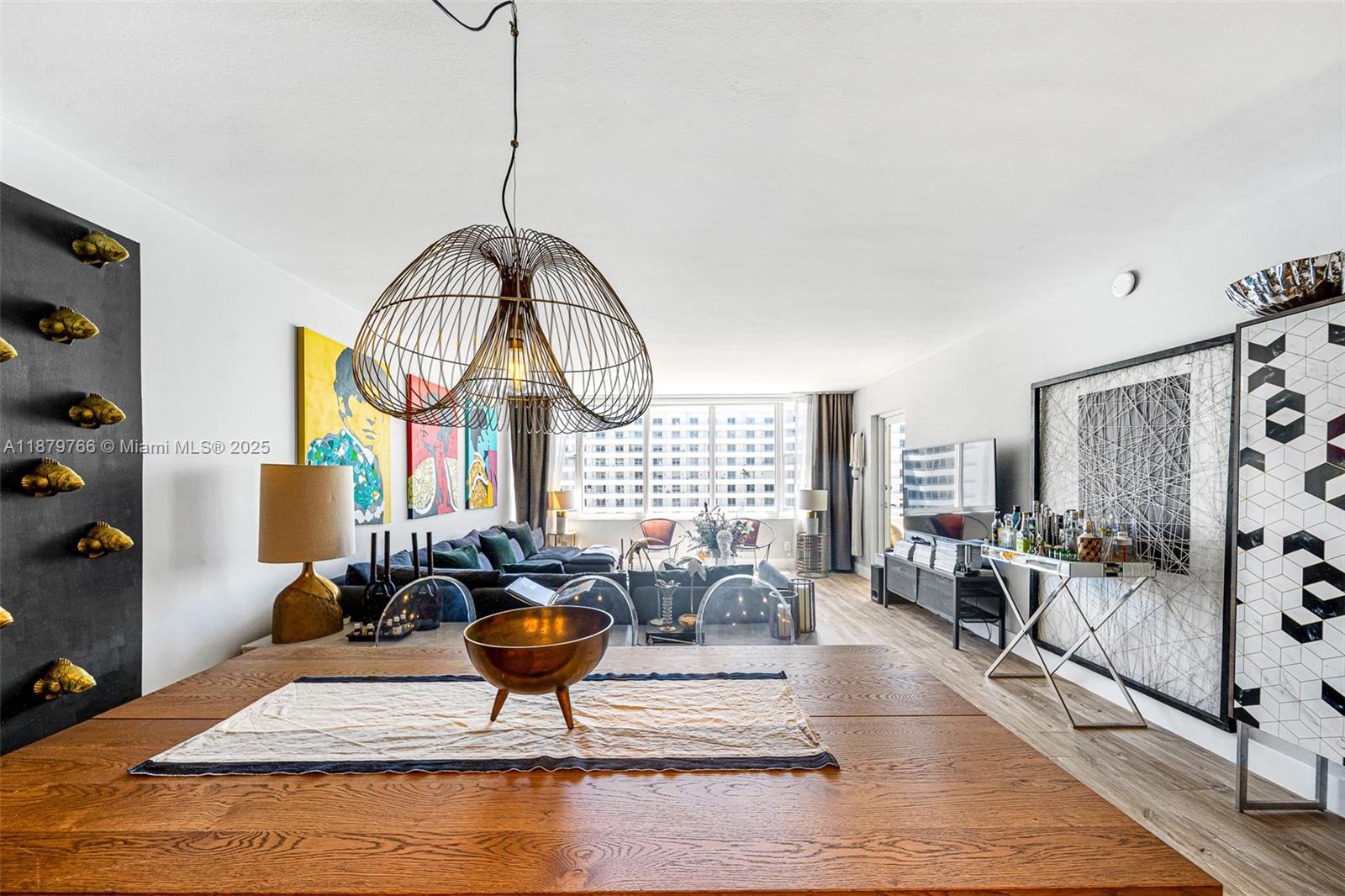 A dining area with a wooden table and wire pendant light overlooks a living room — 5600 Collins Ave # 12E, Miami Beach FL 33140, MIAMI BEACH, FL