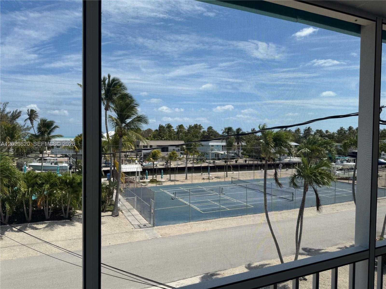 A view from a screened balcony overlooking a tennis court, palm trees, and a canal — 118 Cortez Dr # B, Islamorada FL 33036, ISLAMORADA, FL