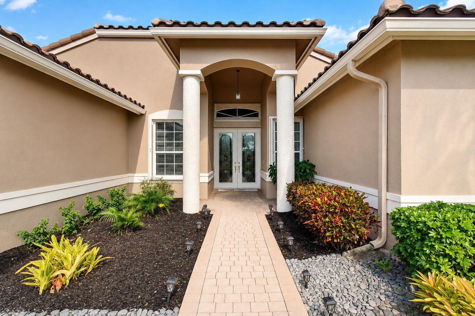 A paved walkway leads to the front entrance of a tan house with two white columns — 8969 Torcello Way, Boynton Beach FL 33472, BOYNTON BEACH, FL