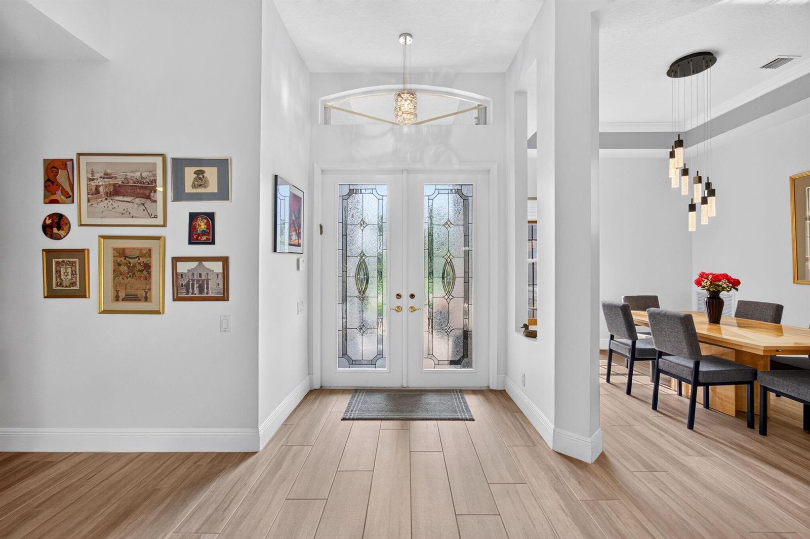 An entryway with double glass doors, light wood-look tile floors, and an adjacent dining area — 8969 Torcello Way, Boynton Beach FL 33472, BOYNTON BEACH, FL
