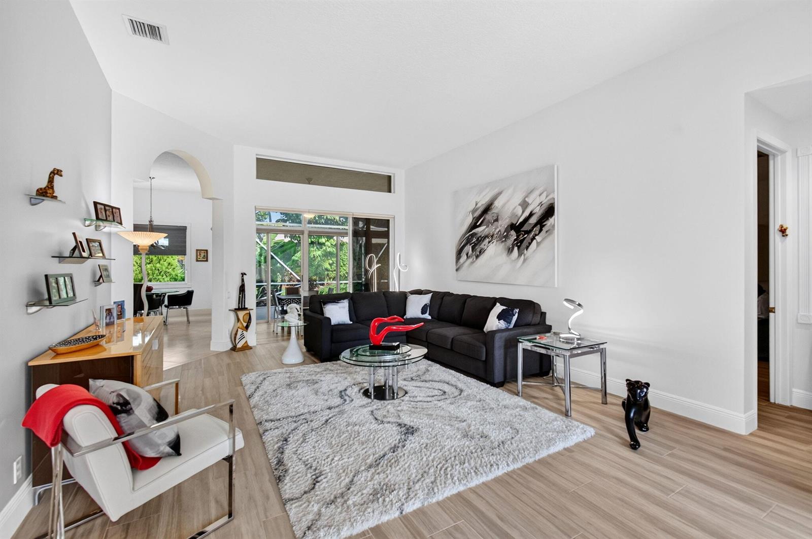 A living room features a dark sectional sofa, a glass coffee table, and light wood-look flooring — 8969 Torcello Way, Boynton Beach FL 33472, BOYNTON BEACH, FL
