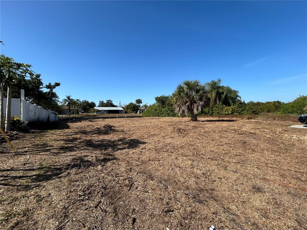 A vacant, cleared lot features dry grass, a single palm tree, and a white fence — 3285 SANTA BARBARA DR, PUNTA GORDA, FL
