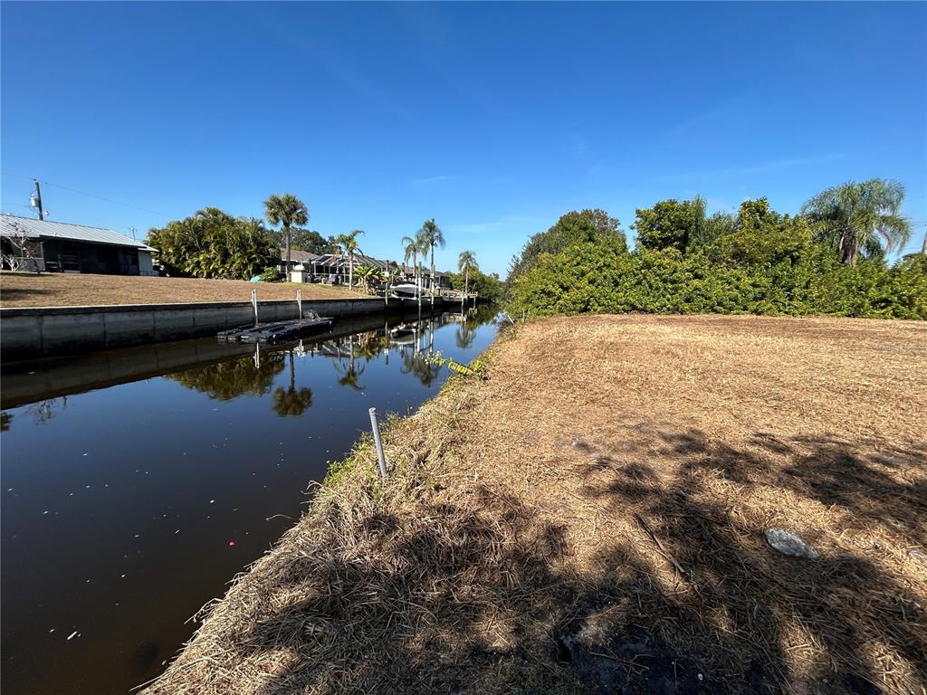 A canal runs alongside a vacant, grassy lot with trees and houses in the distance — 3285 SANTA BARBARA DR, PUNTA GORDA, FL