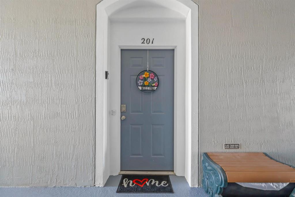 A gray front door with a floral wreath and a welcome mat sits under an archway — 2310 SILVER PALM DRIVE UNIT 201, KISSIMMEE, FL