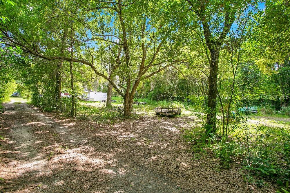 A dirt path leads through a wooded area with a small trailer parked in the clearing — 8816 TREVARTHON ROAD, ORLANDO, FL