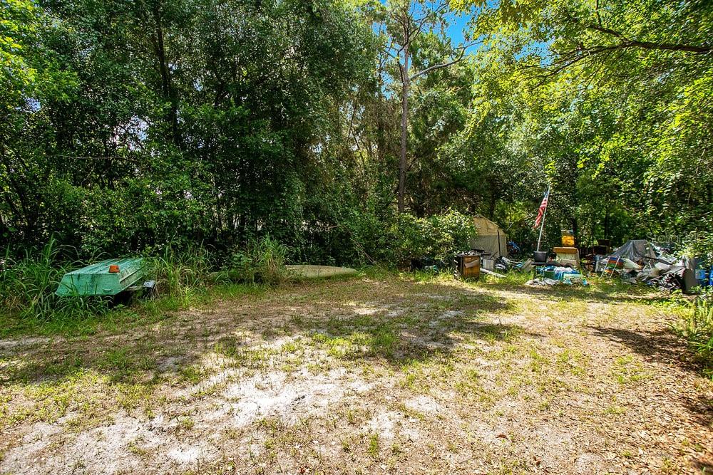 A grassy, wooded lot features a small green boat and various items near the trees — 8816 TREVARTHON ROAD, ORLANDO, FL