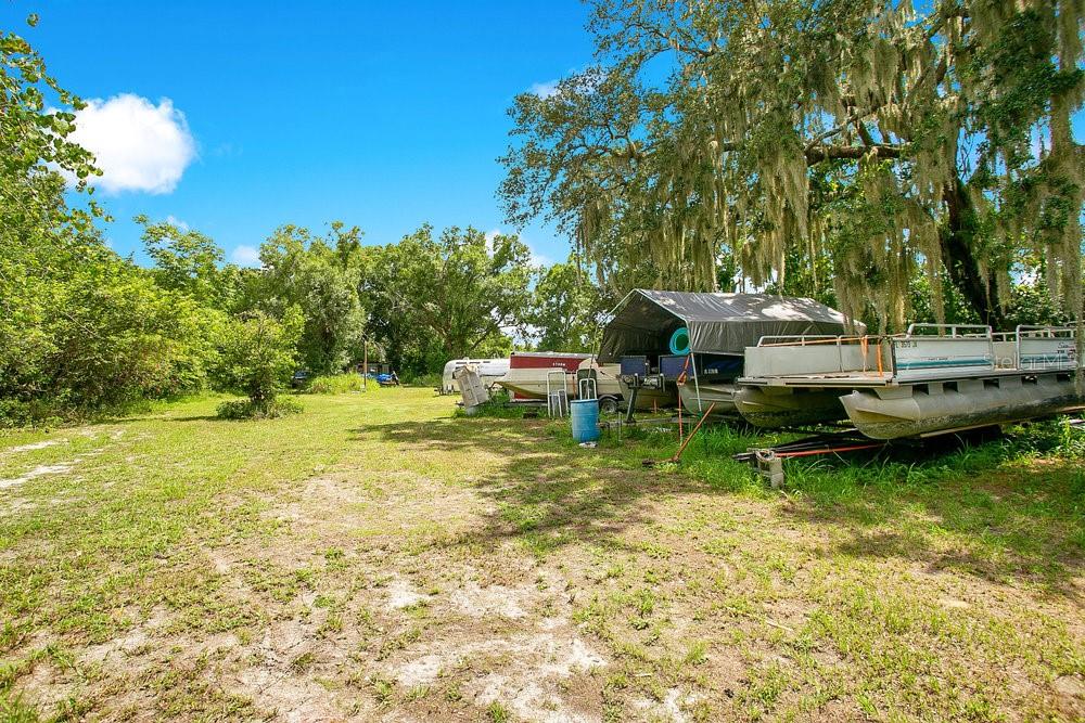 A grassy yard features several boats parked under a canopy and large mossy oak trees — 8816 TREVARTHON ROAD, ORLANDO, FL
