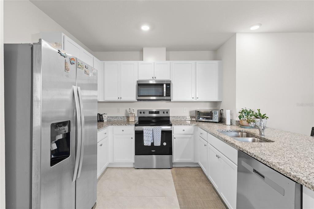 A kitchen features white cabinets, granite countertops, stainless steel appliances, and a tile floor — 1452 CUMBERLAND AVENUE, DAVENPORT, FL
