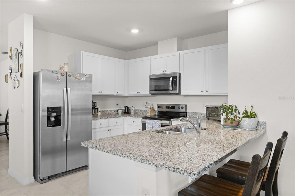 A kitchen features white cabinets, granite countertops, stainless steel appliances, and a breakfast bar — 1452 CUMBERLAND AVENUE, DAVENPORT, FL