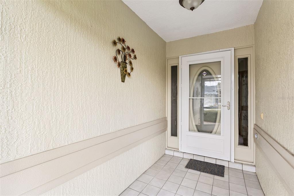 A covered entryway features a white storm door, tiled flooring, and textured beige walls — 501 EASTLAKE DRIVE, HAINES CITY, FL