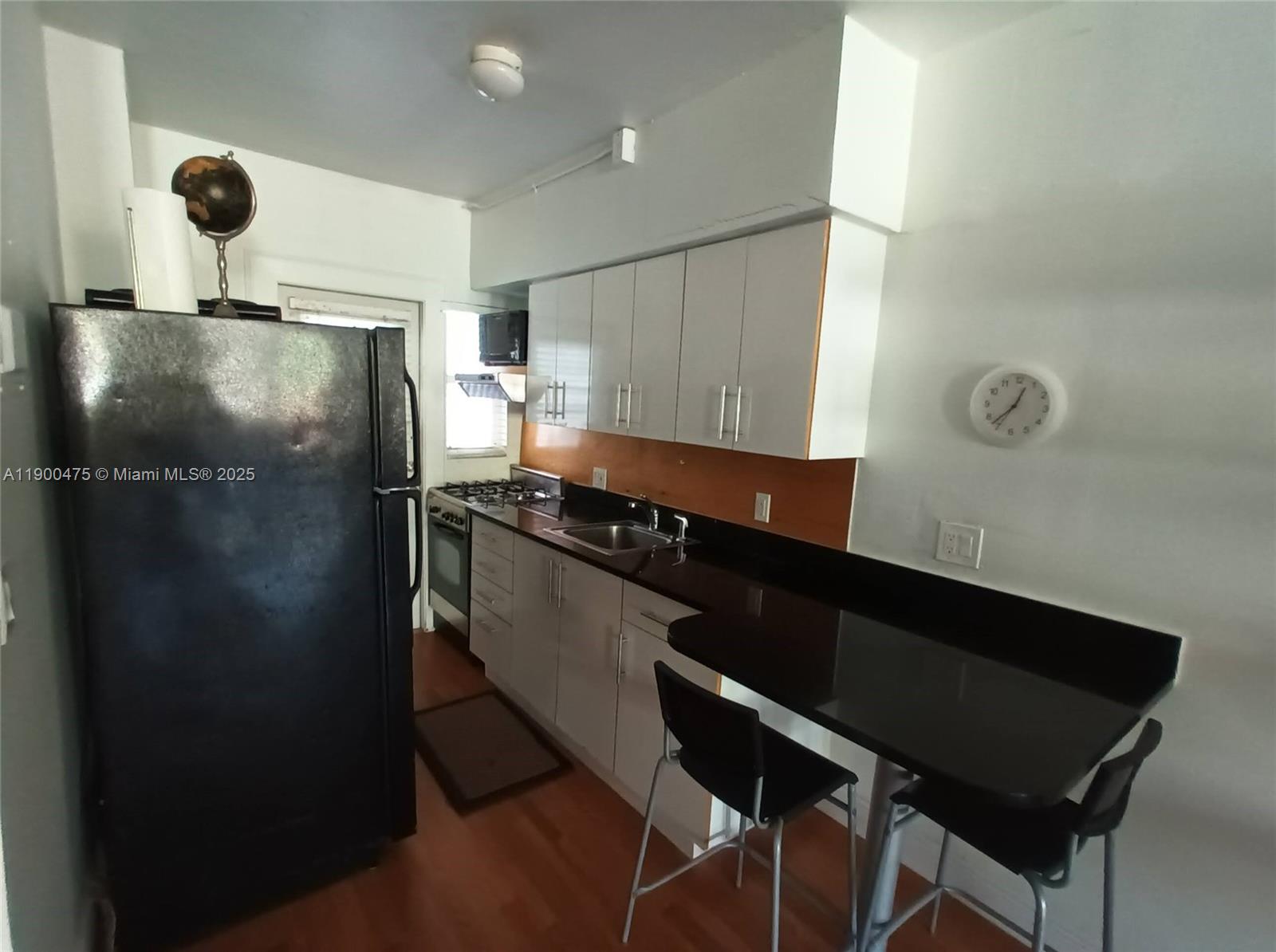 A kitchen features white cabinets, black countertops, a black refrigerator, and a breakfast bar — 300 74th St # 3, Miami Beach FL 33141, MIAMI BEACH, FL