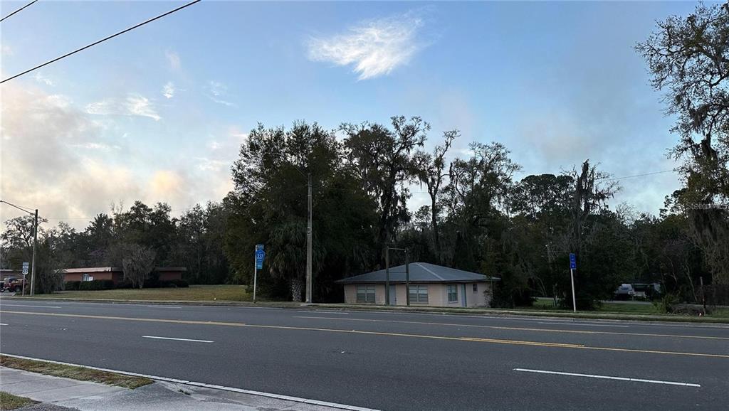 A view of a single-story house situated behind a multi-lane road and trees — 602 HATHAWAY AVENUE, BRONSON, FL