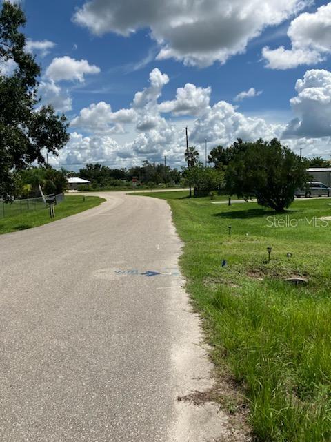 A paved road leads through a grassy residential area under a bright, cloudy sky — 2011 CALLE BONITO, PUNTA GORDA, FL