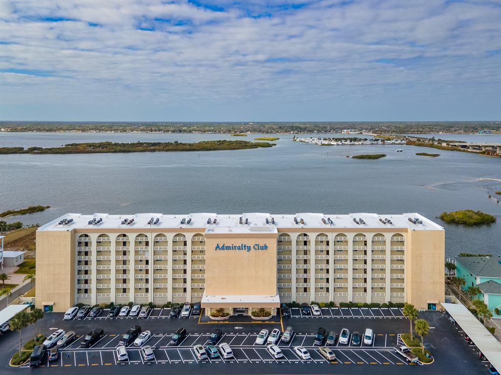 An aerial view shows the Admiralty Club apartment building with a parking lot and waterfront — 3606 S PENINSULA DRIVE UNIT 208, PORT ORANGE, FL