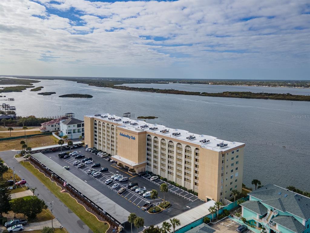 An aerial view shows the Admiralty Club apartment building with a parking lot and waterfront — 3606 S PENINSULA DRIVE UNIT 208, PORT ORANGE, FL