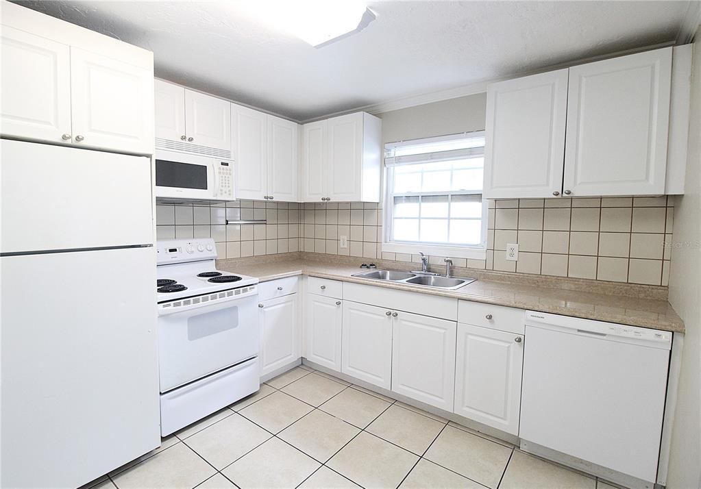 A kitchen features white cabinets, white appliances, beige tile countertops, and light-colored floor tiles — 1638 REDWOOD STREET UNIT 1, SARASOTA, FL