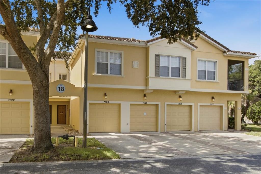 A row of yellow two-story townhouses with attached garages and a large tree in front — 7524 BLISS WAY UNIT 7524, KISSIMMEE, FL