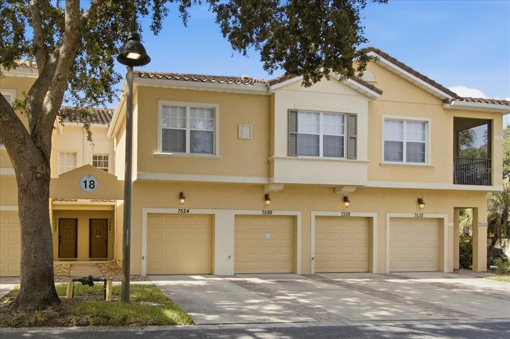 A multi-unit townhouse building with beige stucco walls, four garage doors, and a tree — 7524 BLISS WAY UNIT 7524, KISSIMMEE, FL